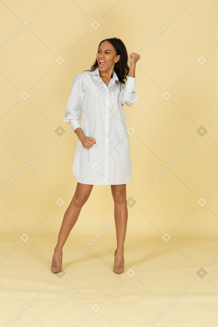 Front view of a screaming dark-skinned young female in white dress clenching fists