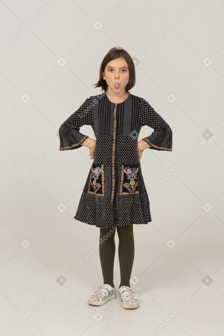 Front view of a funny little girl in dress showing tongue and putting hands on hips