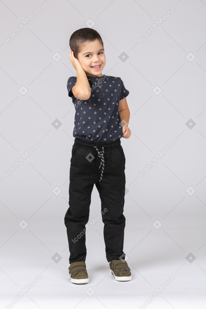 Front view of a happy boy covering ear with hand and looking at camera