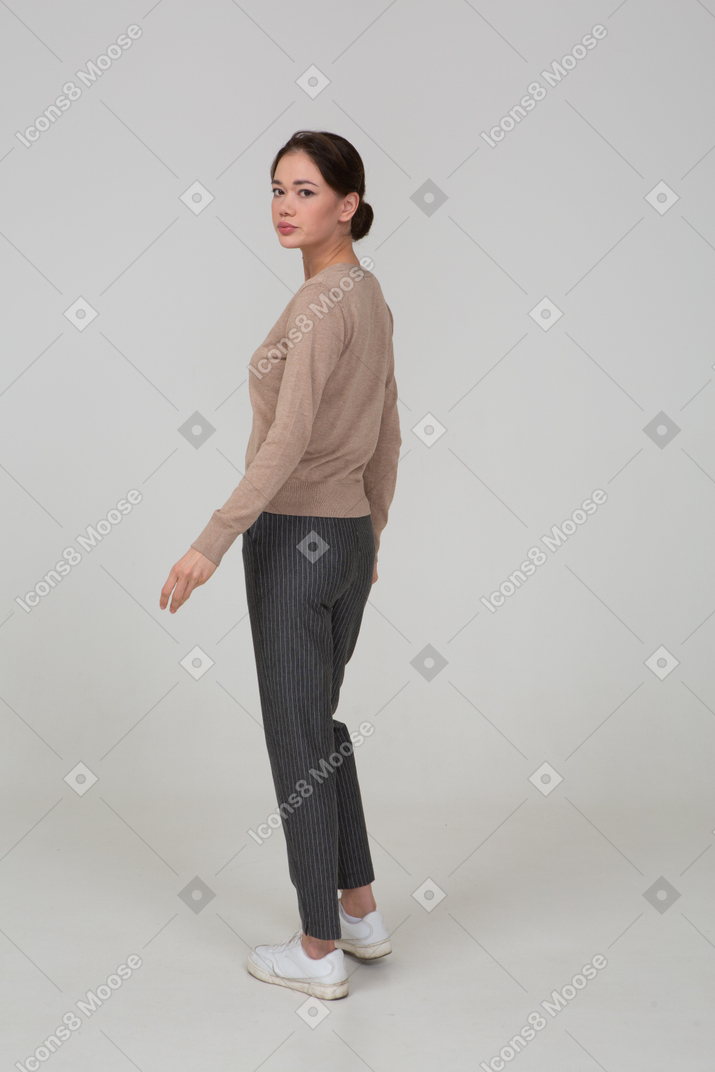 Three-quarter back view of a young lady in beige pullover walking away