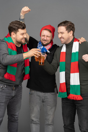 Вид спереди трех футбольных фанатов мужского пола, празднующих победу