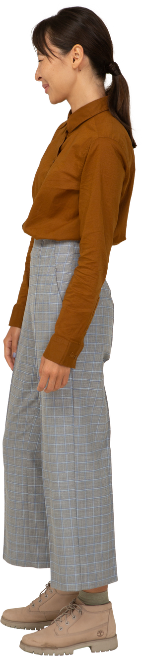 Vista laterale di una giovane donna asiatica ammiccante in calzoni e camicetta