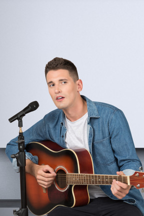 A man sitting in front of a microphone holding a guitar