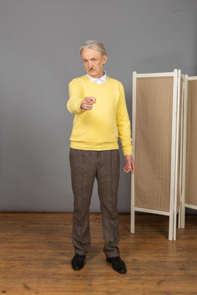 Vista frontal de un anciano apuntando con el dedo mientras mira a la cámara