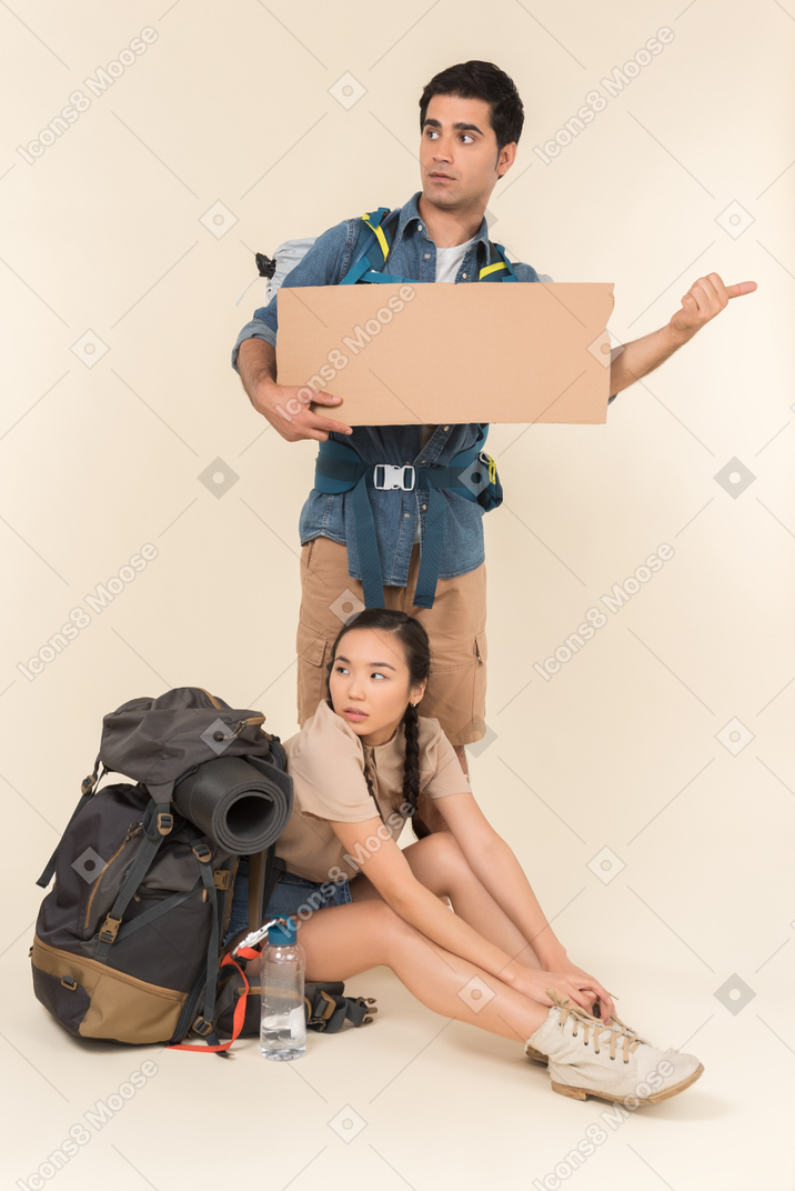 Slightly scared looking interracial couple of hitchhikers holding paper card