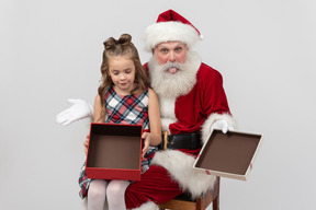 Muchacha triste del niño que sostiene la caja de regalo vacía y santa que muestra una lengua