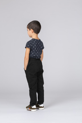 Вид сзади симпатичного мальчика в повседневной одежде, позирующего с руками в кармане