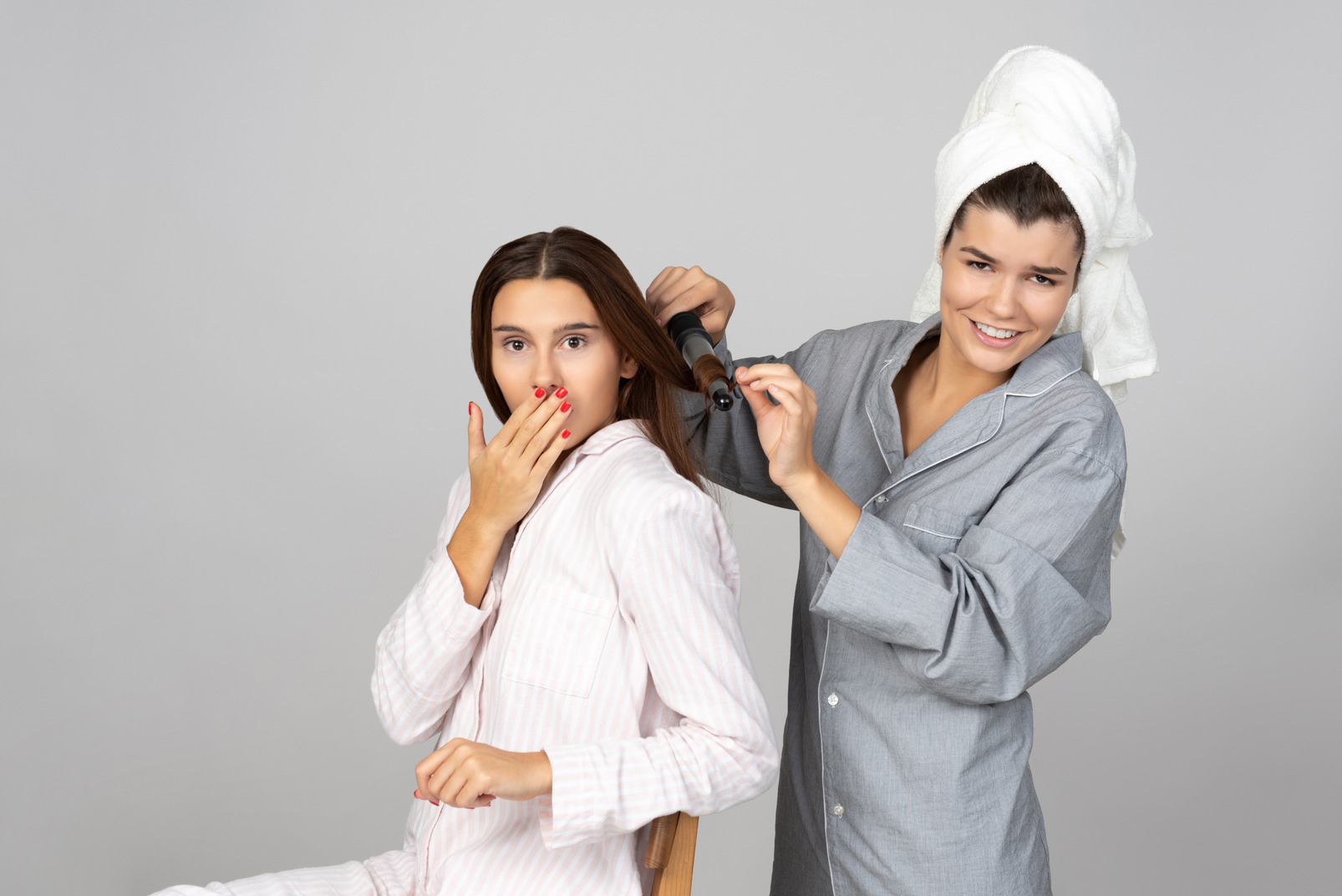 Woman styling her friend's hair with hairstyling iron