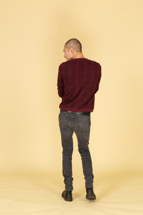 Вид сзади на молодого человека в красном пуловере, смотрящего в сторону
