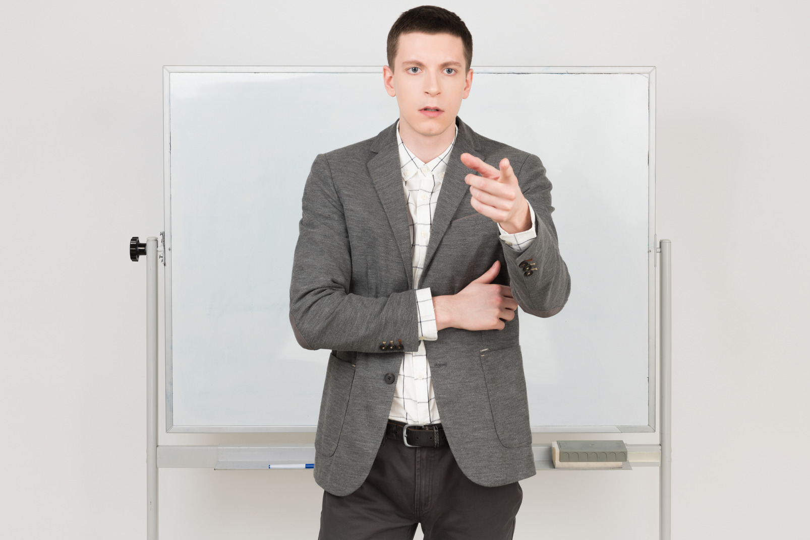 Young handsome man standing next to a whiteboard and pointing at something