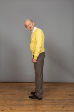 Вид сбоку удивленного старика в желтом пуловере, наклонившегося и смотрящего в камеру