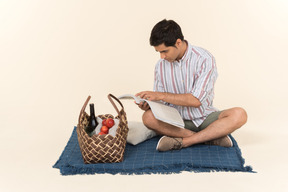 Young caucasian guy sitting on blanket and holding magazine opened