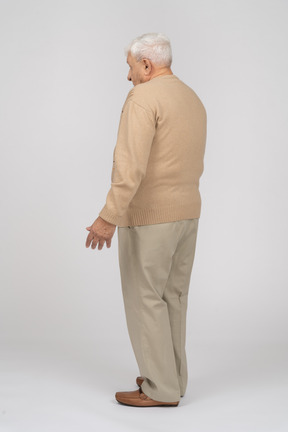 Вид сбоку на растерянного старика в повседневной одежде, стоящего с протянутыми руками