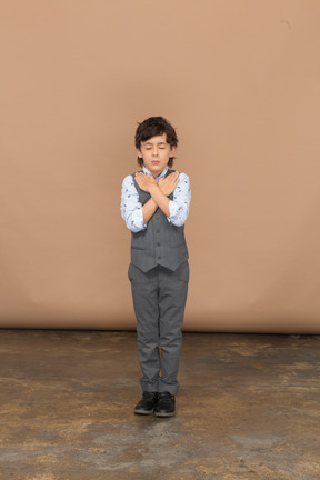 Вид спереди на симпатичного мальчика в костюме, стоящего с руками на плечах