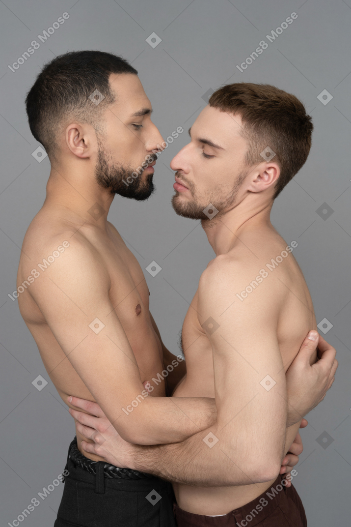 Primo piano di due uomini caucasici a torso nudo in piedi molto vicini e che si toccano delicatamente