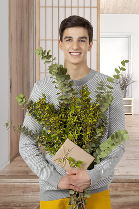 A man holding a small package and a greenery bouquet