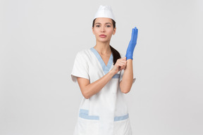 Enfermera atractiva en una bata médica poniéndose un guante de látex
