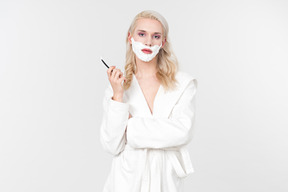 A good looking blond-haired young man in a white bathrobe, being in the process of his beauty care routine