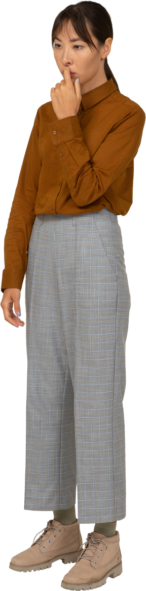 Vista de tres cuartos de una joven mujer asiática en calzones y blusa tocando la boca