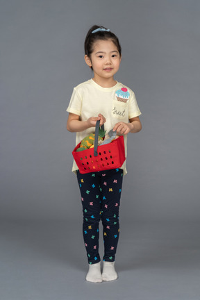 Vista frontal de una niña sosteniendo una cesta de la compra
