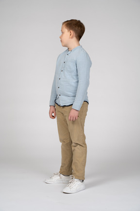 Вид сбоку на мальчика в повседневной одежде, стоящего на месте и смотрящего в сторону