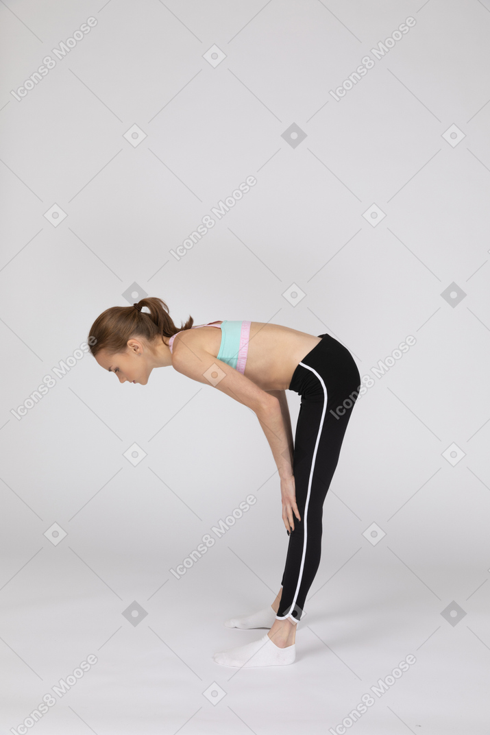 Vista lateral de una jovencita en ropa deportiva en cuclillas y poniendo las manos en las caderas