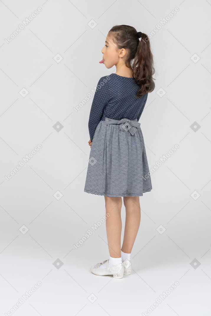 Vista trasera de tres cuartos de una niña que muestra la lengua burlonamente hacia un lado