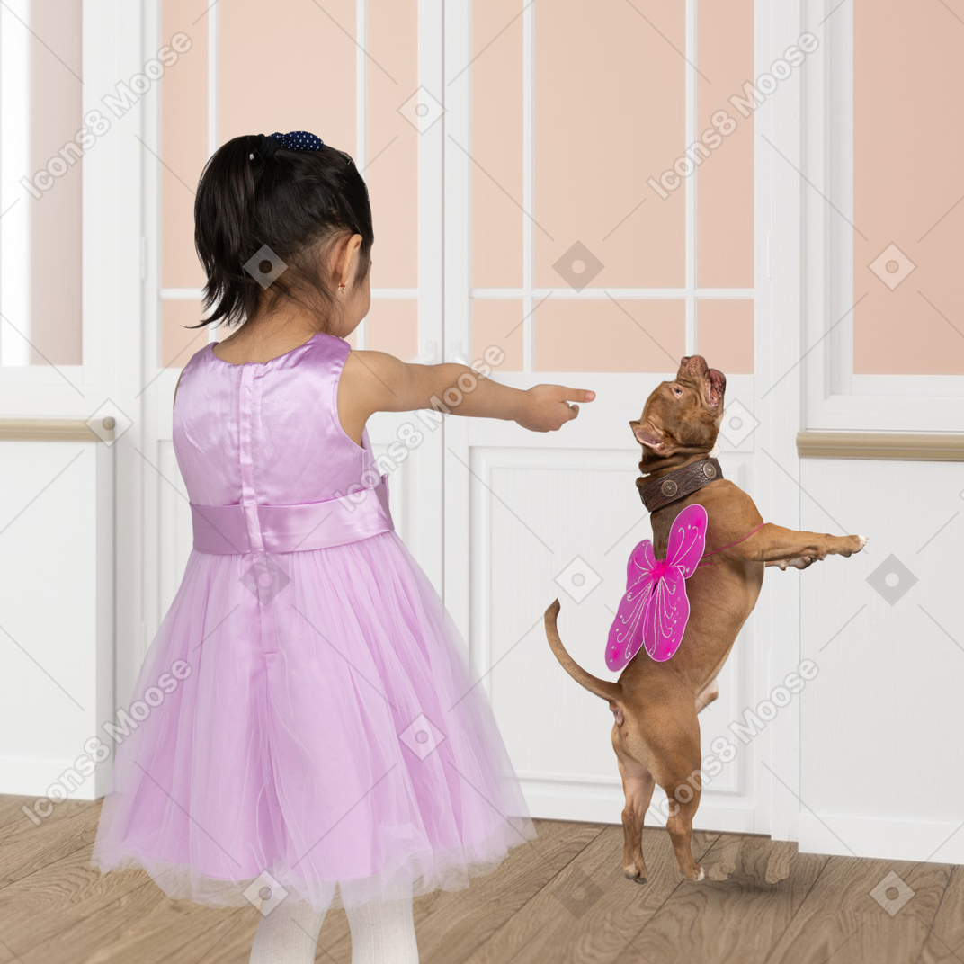 A little girl in a purple dress pointing at a dog with wings