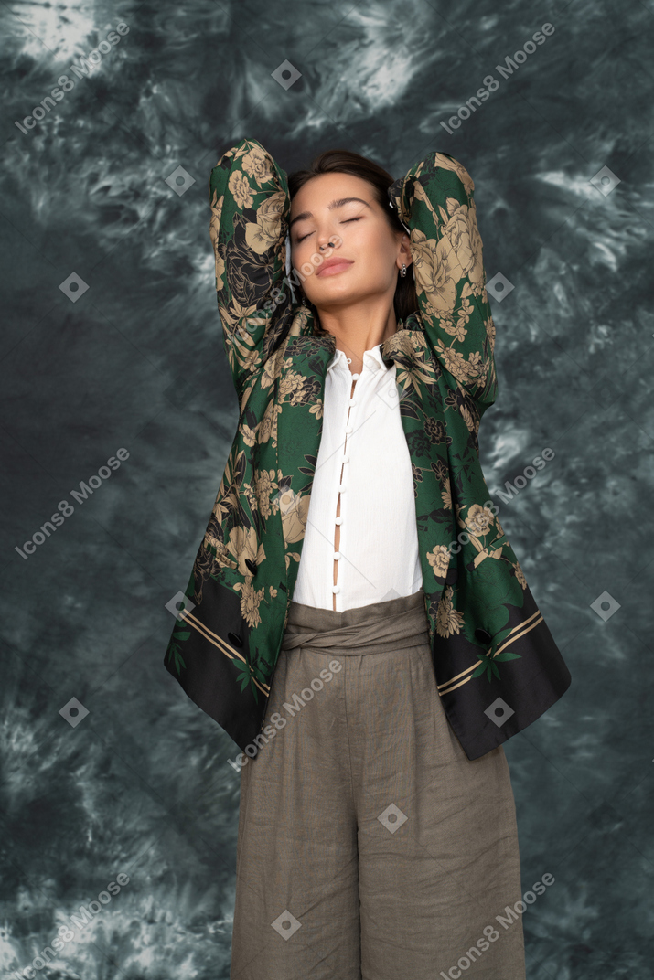 Front portrait of young woman in silk jacket holding hands behind head