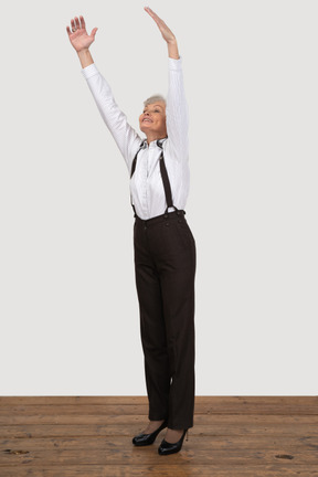 Three-quarter back of an old lady in office clothing raising her hands