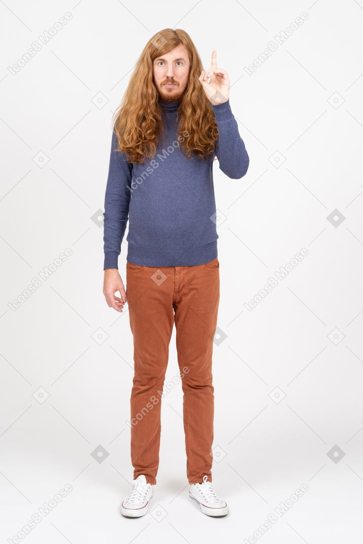 Vorderansicht eines jungen mannes in freizeitkleidung, der mit einem finger nach oben zeigt
