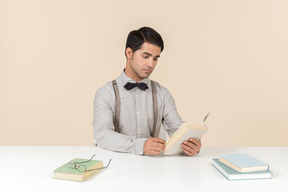 Jovem professor sentado à mesa e ler um livro