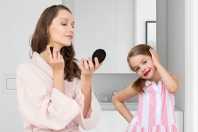 A mother and daughter are putting on makeup in front of a mirror
