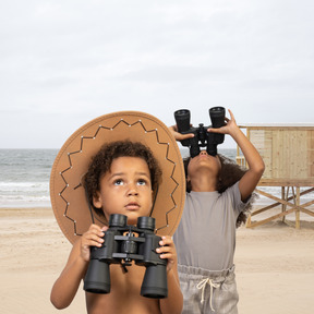 Two children looking through binoculars on the beach