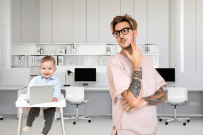 A man with a tattoo on his arm standing next to a baby in a chair