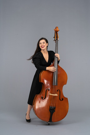 Vista frontale di una giovane donna sorridente in abito nero che suona il contrabbasso