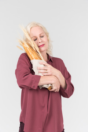 A nice-looking middle-aged blonde woman in a burgundy shirt and with a freshly bought bread in her hands