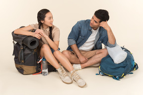 Joven pareja interracial sentado cerca de mochilas y hablando