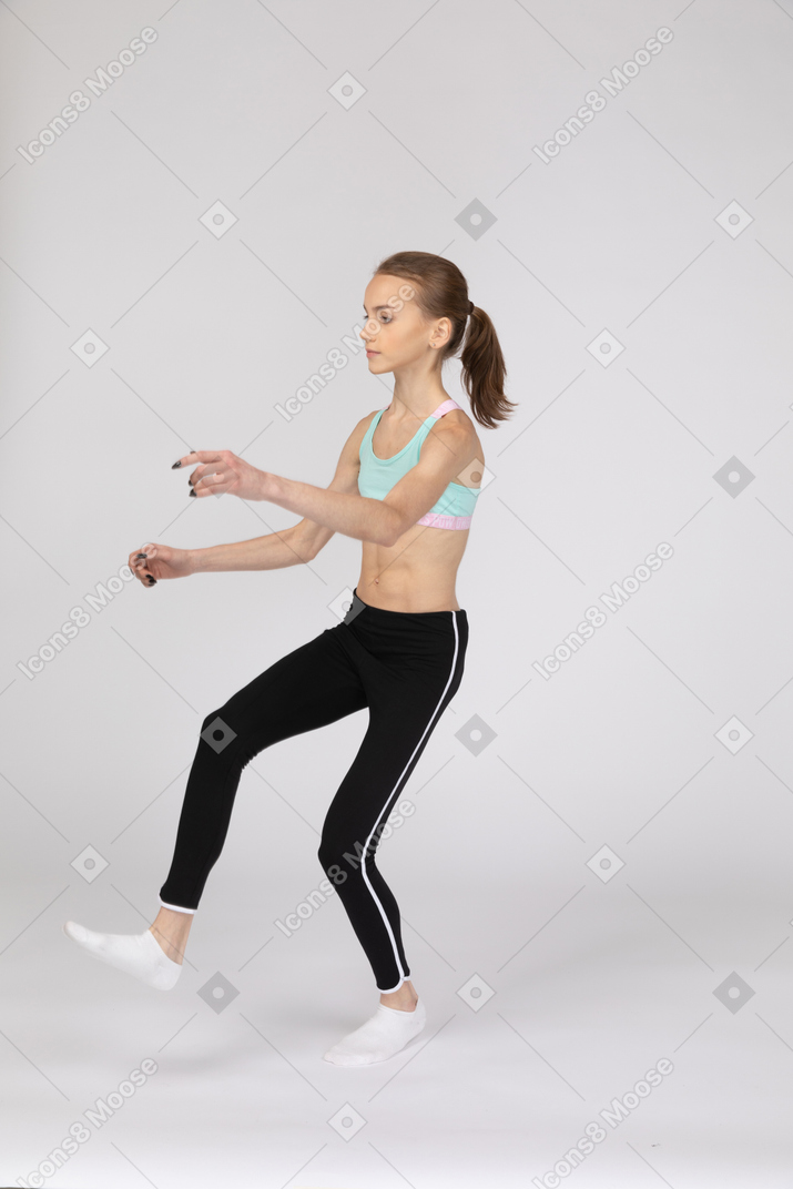 Three-quarter view of a teen girl in sportswear raising hands and leg