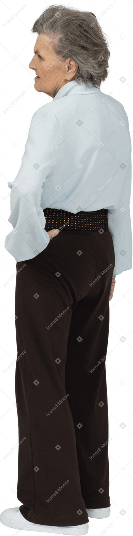 Back view of an old woman in blouse and trousers putting hand on hip