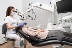 Женщина-стоматолог в полный рост лечит свою пациентку и смотрит в микроскоп