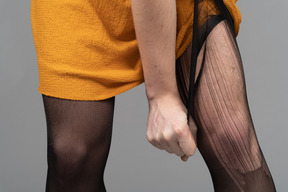 Cropped photo of a person in orange dress ripping tights