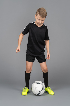 Vista frontal de uma criança menino em uniforme de futebol olhando para a bola