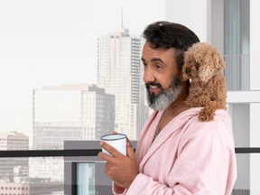 A man with a poodle on his shoulders holding a cup