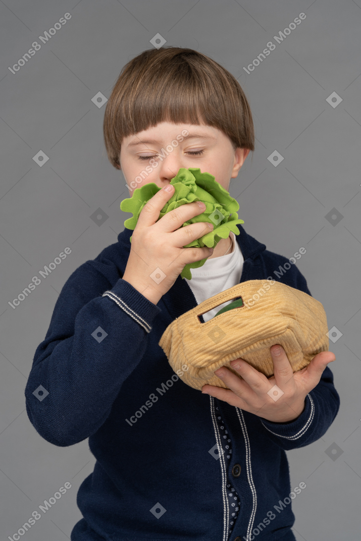 Portrait of a little boy pretending to eat a stuffed cabbage toy