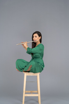 Full-length of a young lady playing the clarinet sitting with her legs crossed on a wooden chair