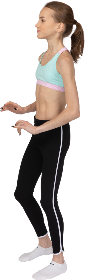 Vista lateral de uma linda garota adolescente em roupas esportivas se afastando e levantando as mãos