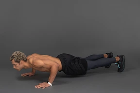 Vista de tres cuartos de un hombre afro sin camisa haciendo flexiones