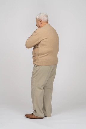 Side view of an old man in casual clothes standing with crossed arms