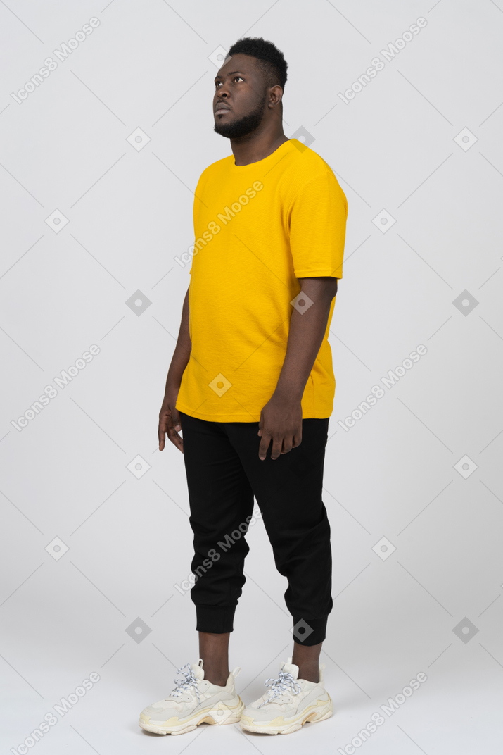 노란색 티셔츠를 입은 어두운 피부의 젊은 남자가 가만히 서 있는 모습